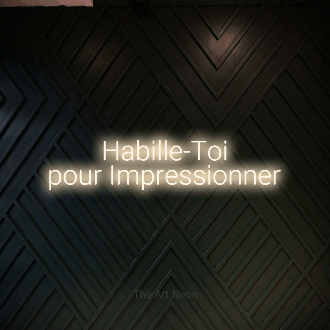“Habille-toi pour impressionner” LED neon sign in warm white, with rounded sans-serif lettering across 2 lines, shown against a black chevron-patterned wood wall.