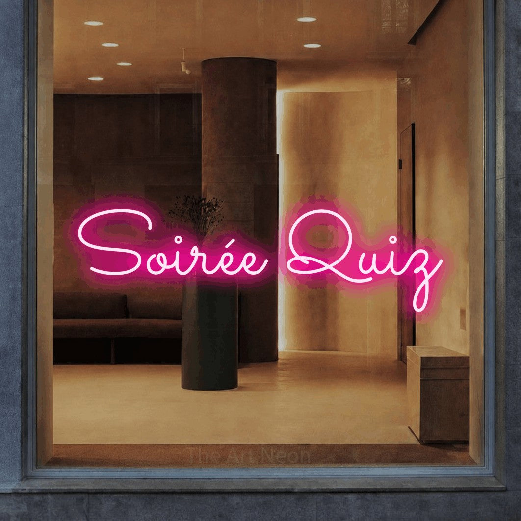 Décoration murale en néon LED « Soirée quiz » en rose vif, en lettres cursives aux boucles marquées, installée dans un intérieur aux tons chauds, pour un bar ou un pub.