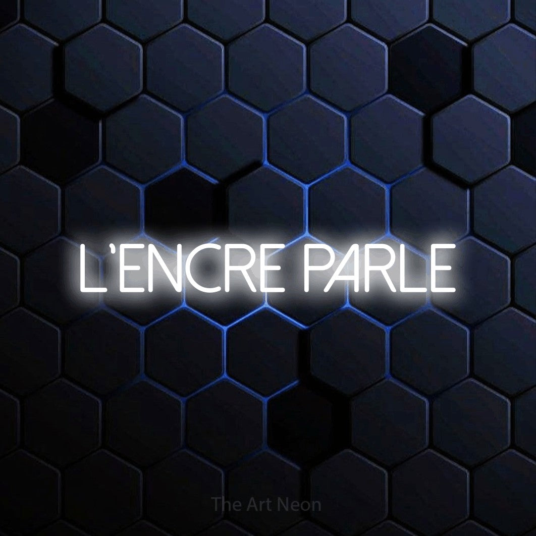 “L'encre parle” LED neon sign in cool white, with thin sans-serif lettering, shown against a dark blue honeycomb pattern.