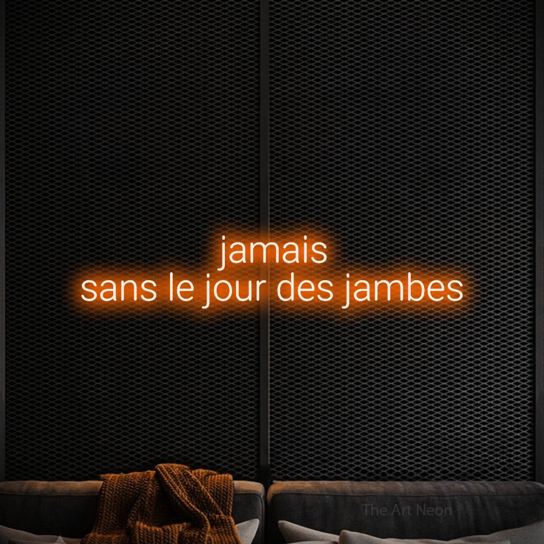“Jamais sans le jour des jambes” LED neon sign in orange, with rounded sans-serif lettering across 2 lines, shown against a modern dark-toned seating area.