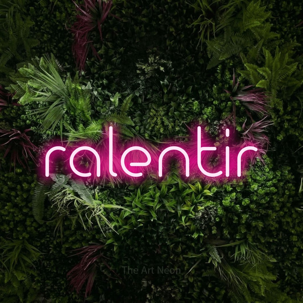 “Ralentir” LED neon sign in hot pink, with stylised geometric lettering, shown against a plant wall with pink flowers.