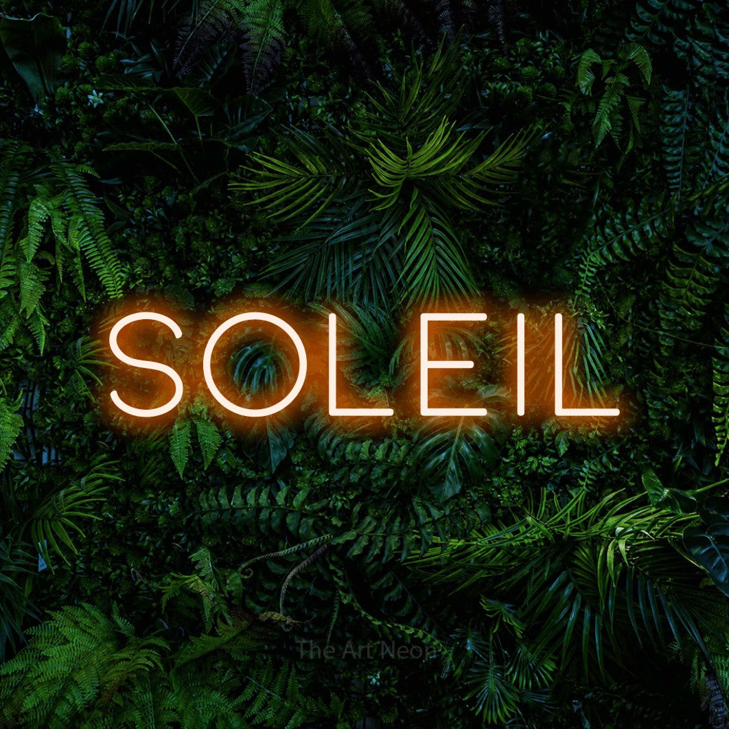 Composition en néon LED « Soleil » en orange, en lettres fines et espacées, mise en valeur devant un feuillage tropical dense, pour un salon.