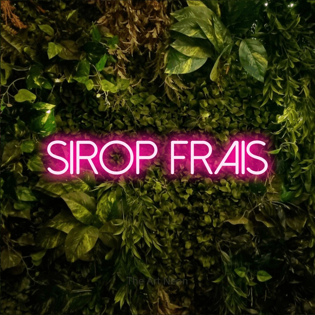 “Sirop frais” LED neon sign in hot pink, with thin sans-serif lettering, shown against bright green and yellow foliage.