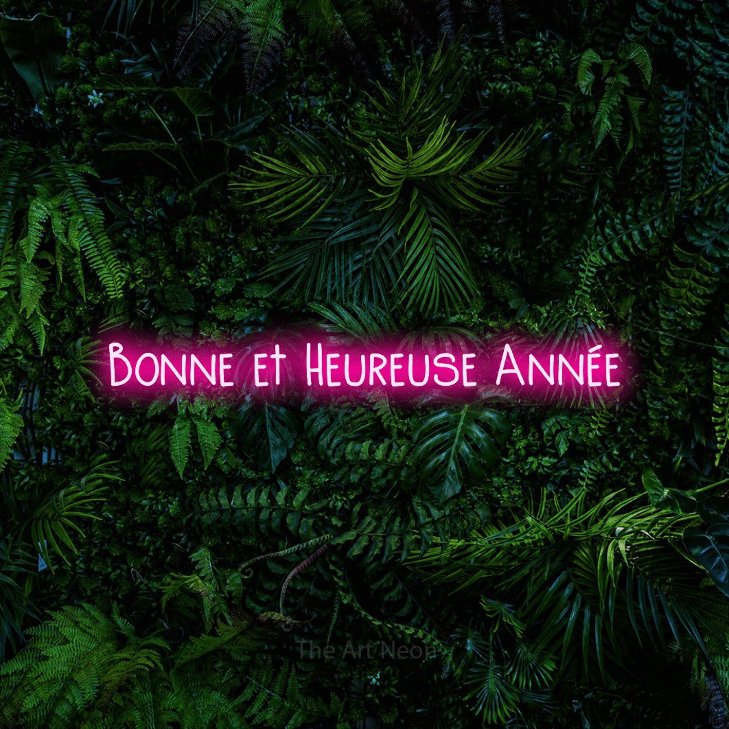 “Bonne et heureuse année” LED neon sign in hot pink, with narrow hand-drawn lettering, shown against dense tropical foliage.