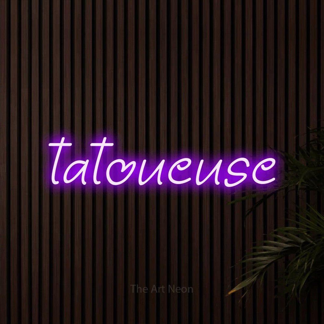 “Tatoueuse” LED neon sign in purple, with slanted handwritten lettering, shown against dark wooden wall slats.