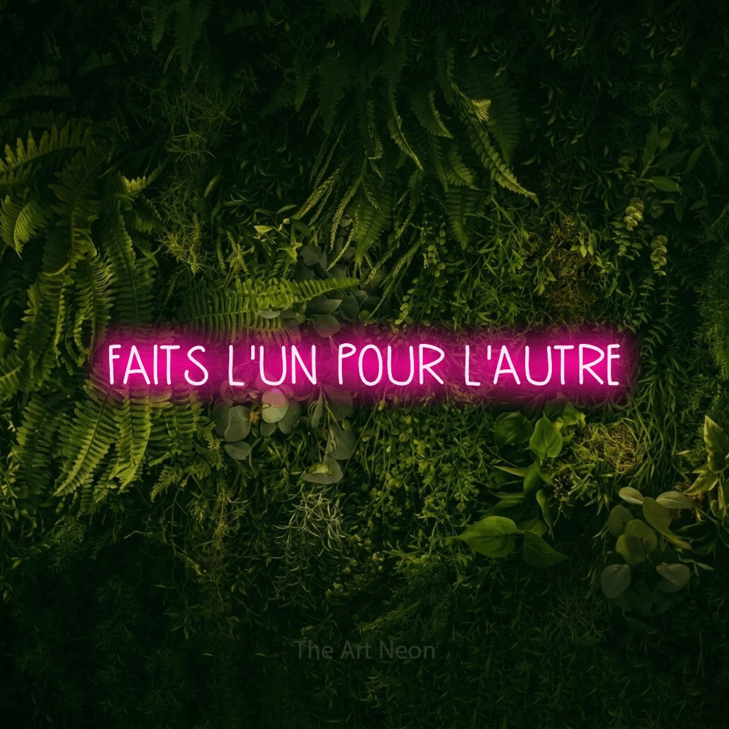 “Faits l'un pour l'autre” LED neon sign in hot pink, with narrow hand-drawn lettering, shown against a dark moss and forest backdrop.