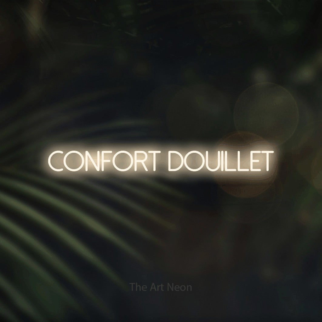 “Confort douillet” LED neon sign in warm white, with thin sans-serif lettering, shown against a blurred palm and bokeh-light backdrop.