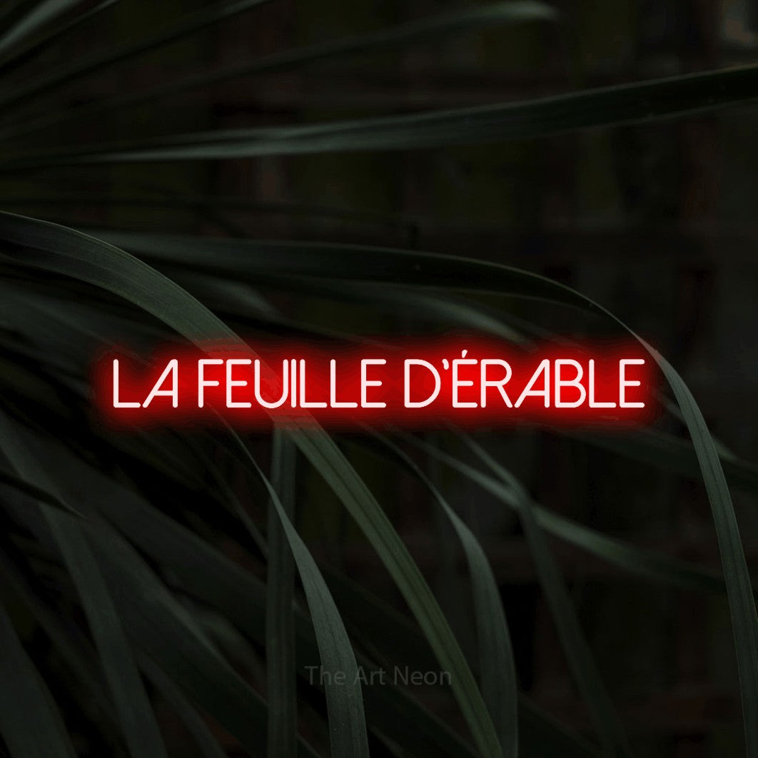 “La feuille d'érable” LED neon sign in red, with thin sans-serif lettering, shown against a close-up of dark foliage.
