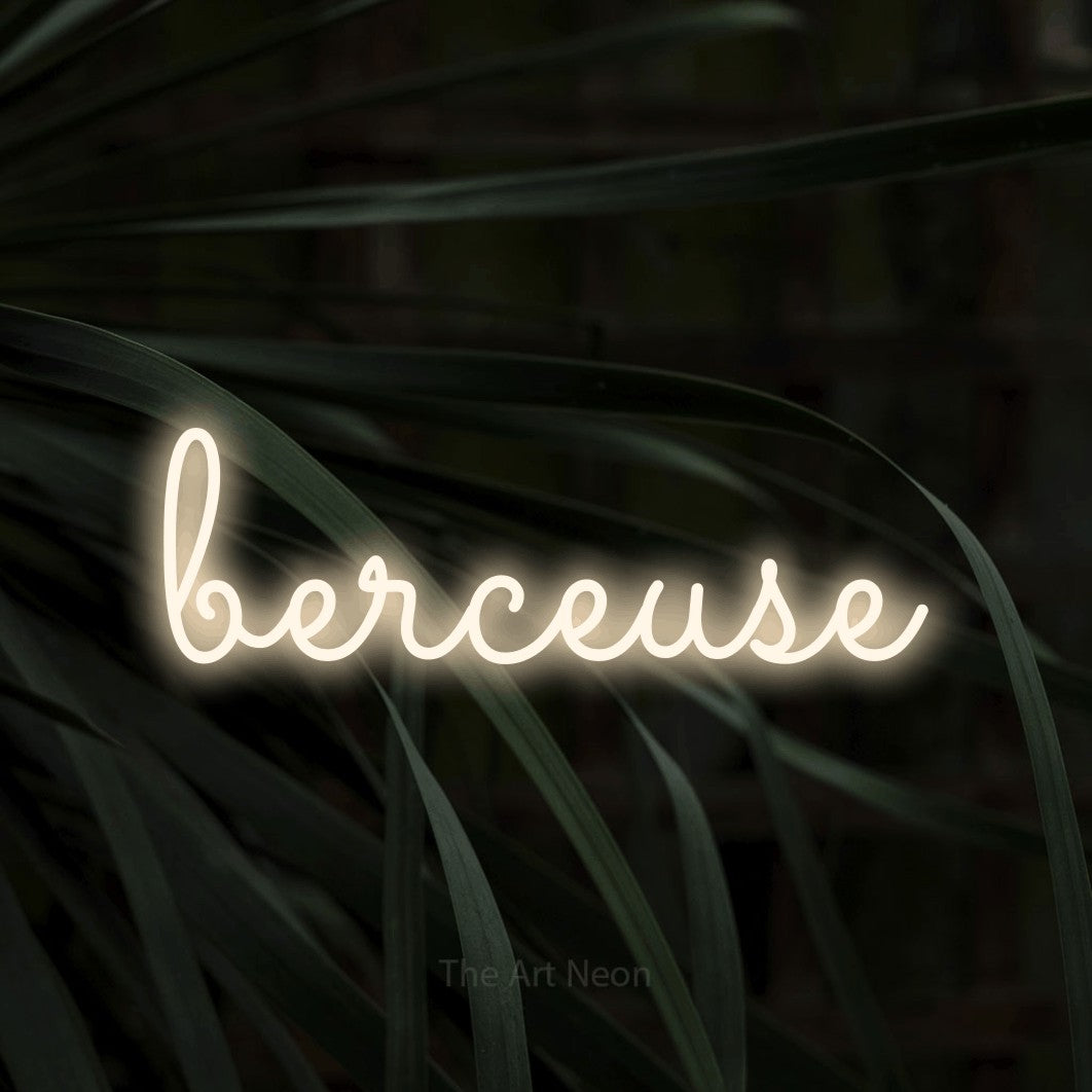 “Berceuse” LED neon sign in warm white, with looped cursive lettering, shown against a close-up of dark foliage.