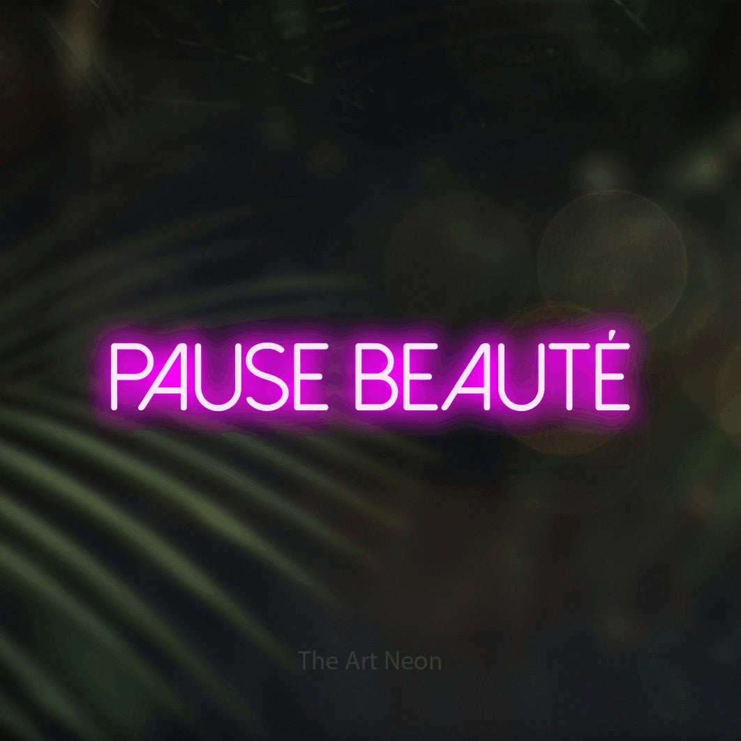“Pause beauté” LED neon sign in pink, with thin sans-serif lettering, shown against a blurred palm and bokeh-light backdrop.