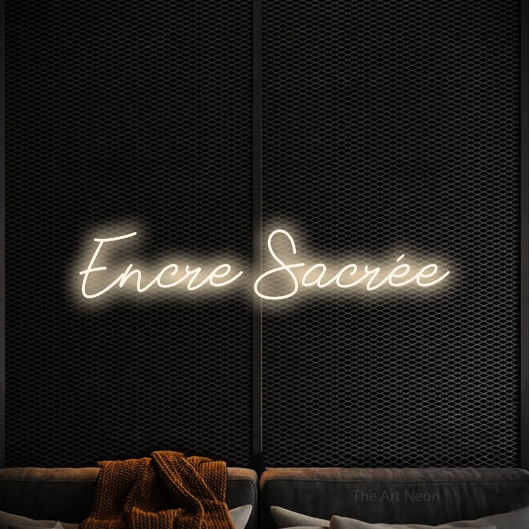 “Encre sacrée” LED neon sign in warm white, with cursive lettering, shown against a modern dark-toned seating area.