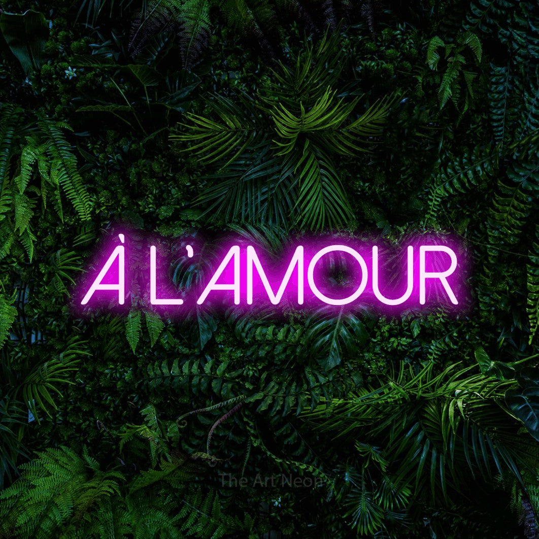 “À l'amour” LED neon sign in pink, with thin sans-serif lettering, shown against dense tropical foliage.