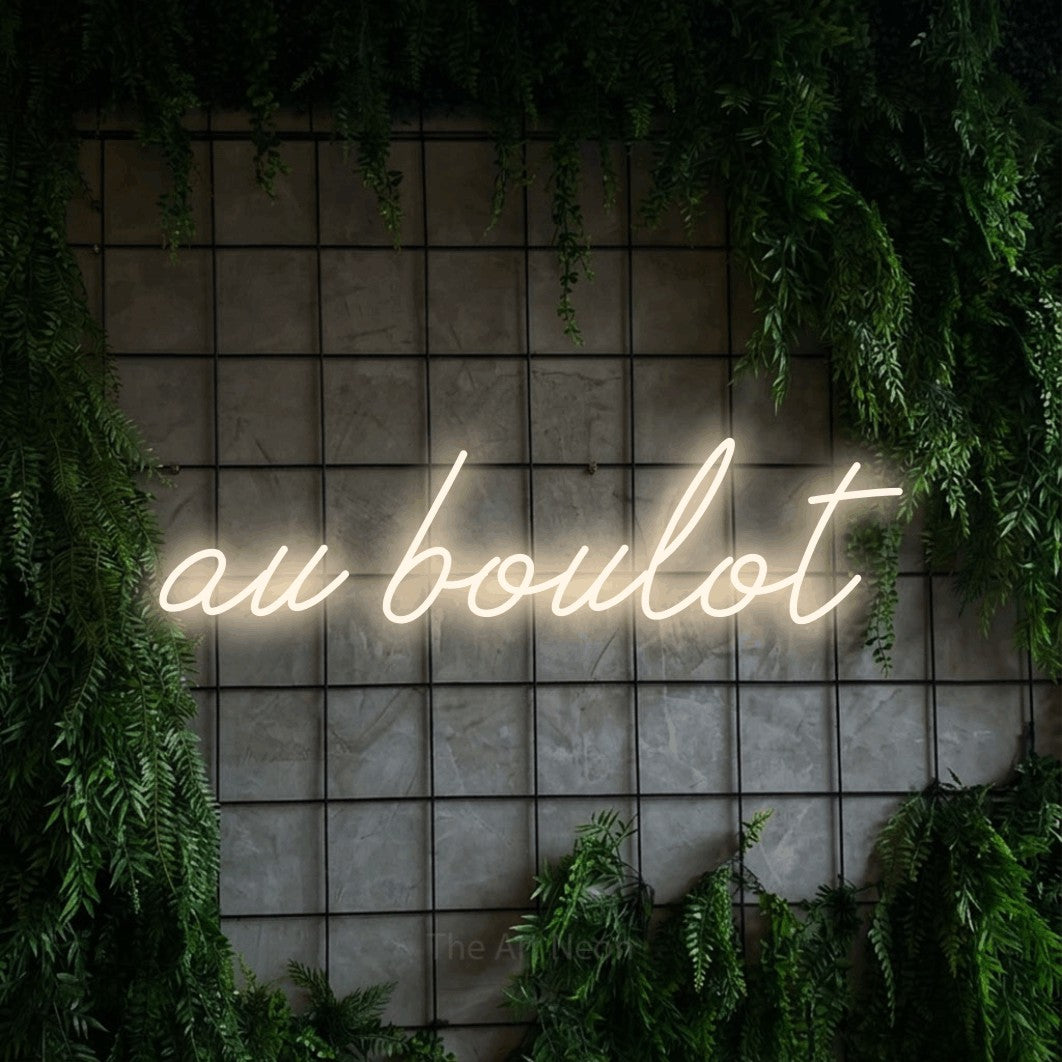 “Au boulot” LED neon sign in warm white, with cursive lettering, shown against an ivy-covered concrete grid.