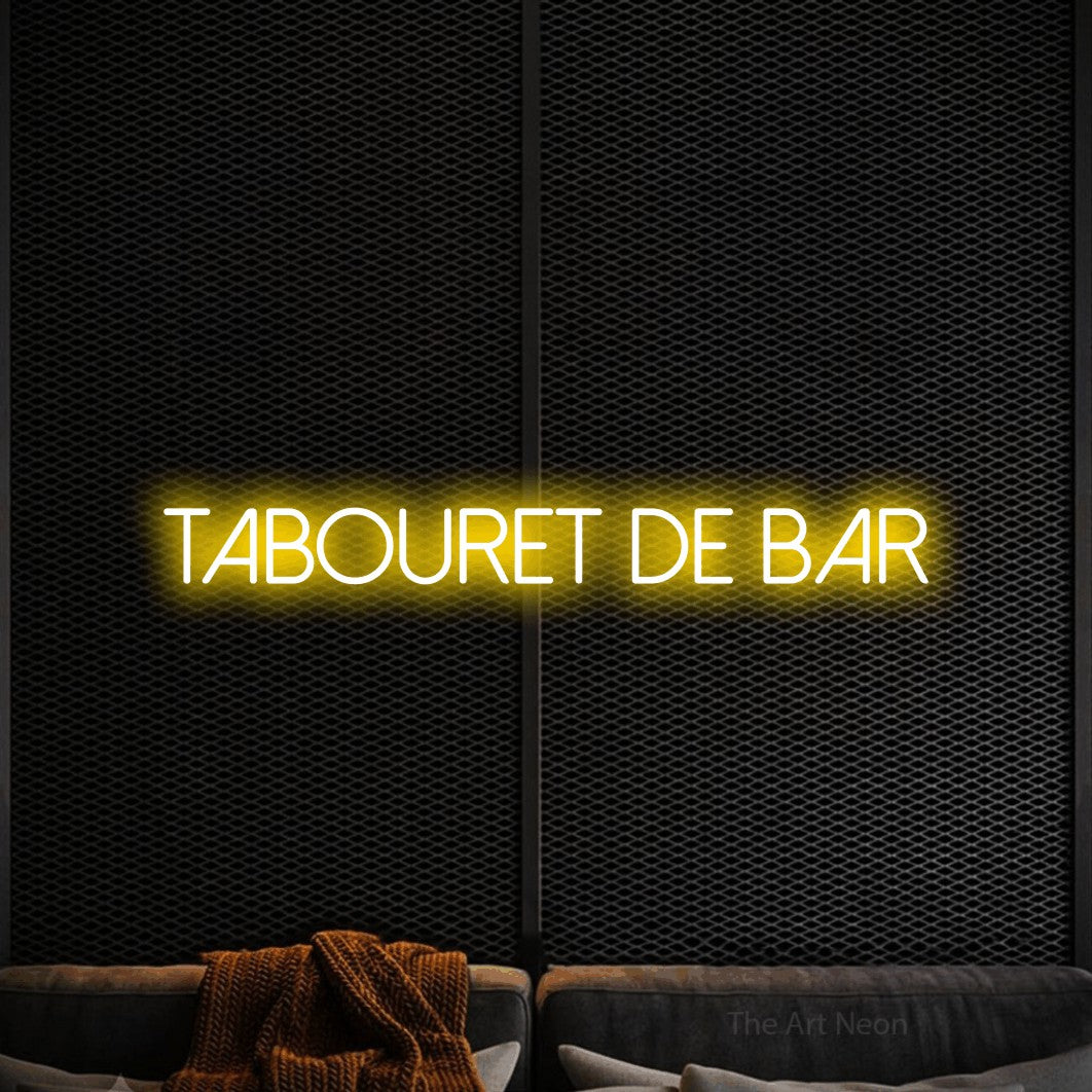 “Tabouret de bar” LED neon sign in yellow, with thin sans-serif lettering, shown against a modern dark-toned seating area.