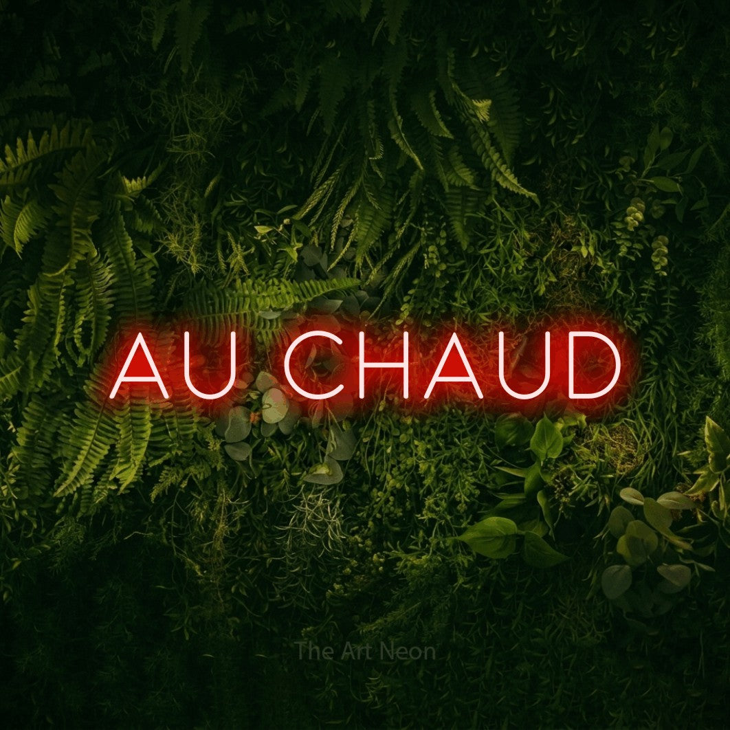 “Au chaud” LED neon sign in red, with thin, widely spaced lettering, shown against a dark moss and forest backdrop.