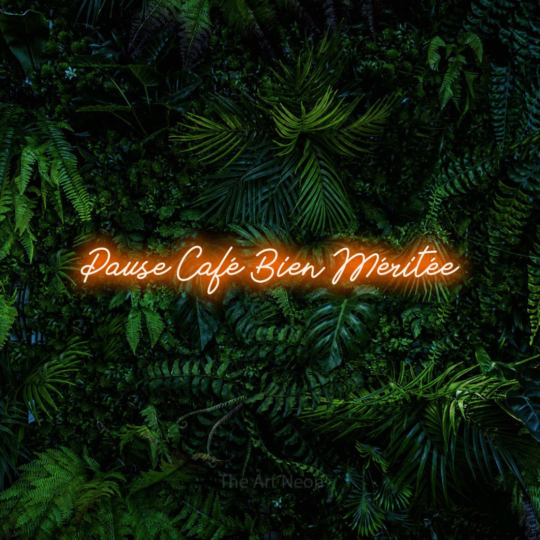 “Pause café bien méritée” LED neon sign in orange, with cursive lettering, shown against dense tropical foliage.