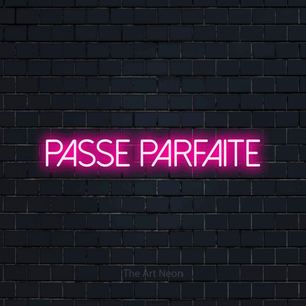 “Passe parfaite” LED neon sign in hot pink, with thin sans-serif lettering, shown against a dark navy brick wall.