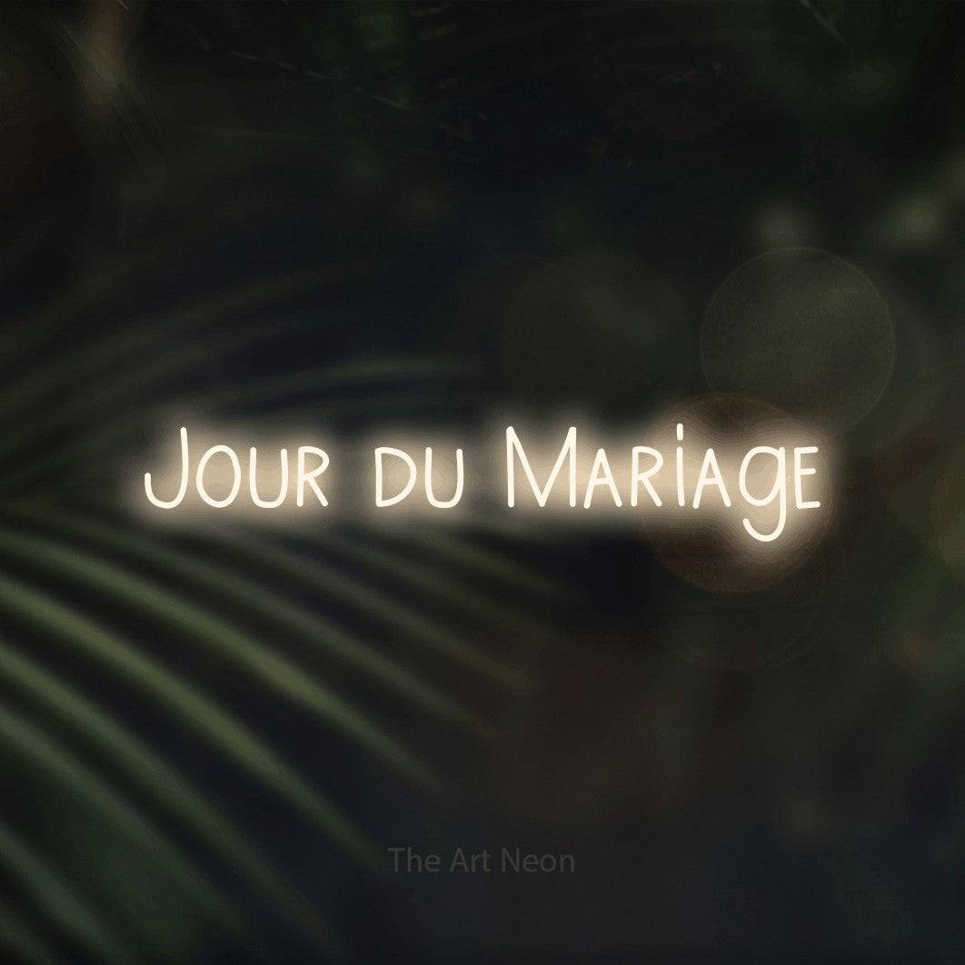 “Jour du mariage” LED neon sign in warm white, with narrow hand-drawn lettering, shown against a blurred palm and bokeh-light backdrop.
