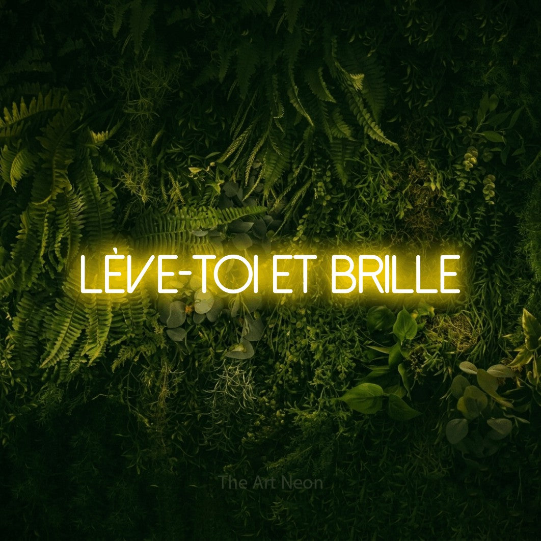 “Lève-toi et brille” LED neon sign in yellow, with thin sans-serif lettering, shown against a dark moss and forest backdrop.