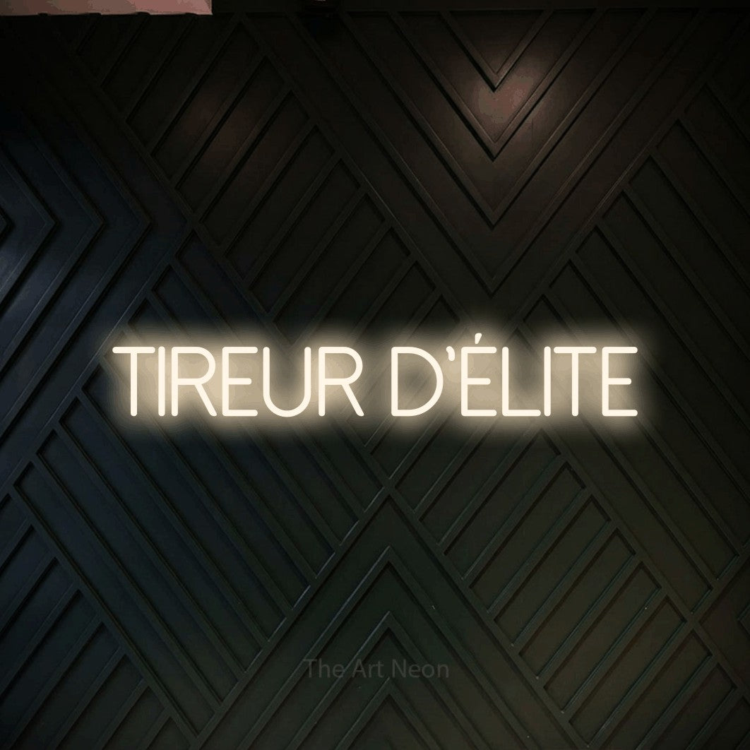 Aperçu d’une enseigne néon LED « Tireur d'élite » en blanc chaud, en lettres fines sans empattement, photographiée sur un mur en bois noir à motif chevron, pour un décor de hockey.