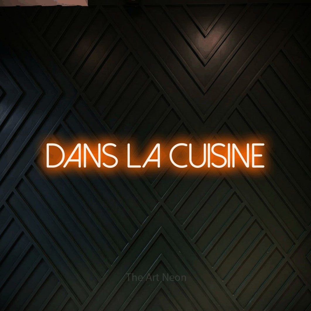 “Dans la cuisine” LED neon sign in orange, with thin sans-serif lettering, shown against a black chevron-patterned wood wall.