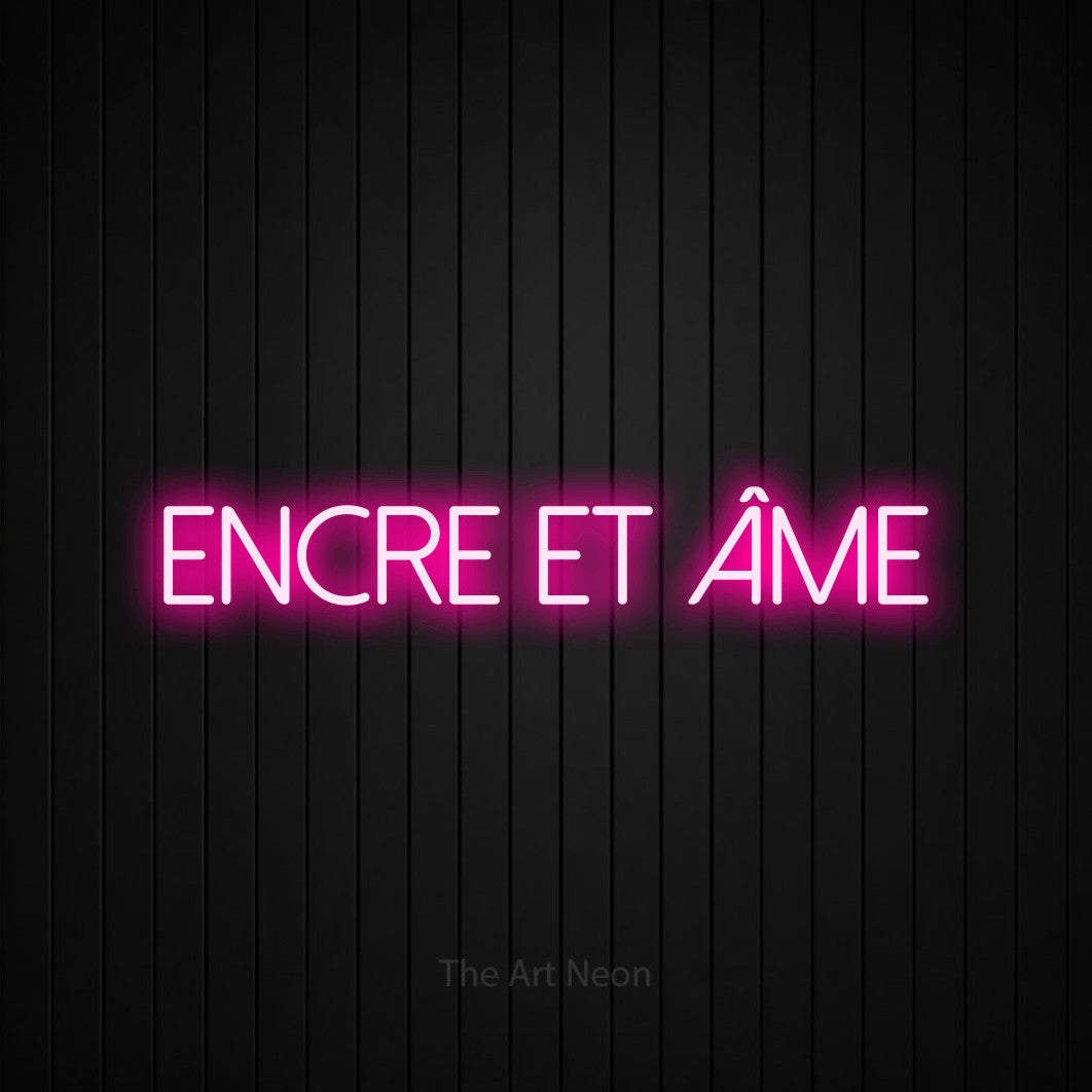 “Encre et âme” LED neon sign in hot pink, with thin sans-serif lettering, shown against black vertical wall slats.