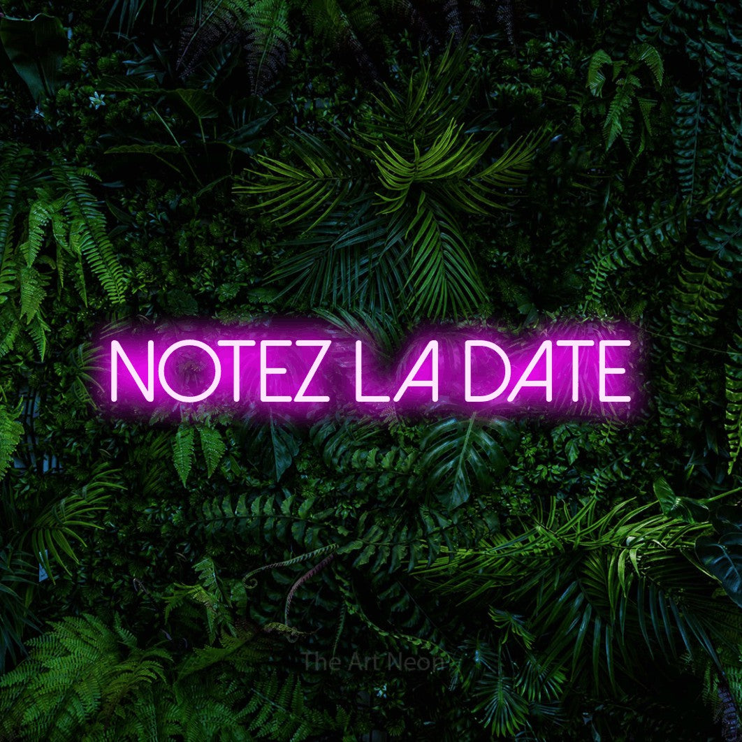 “Notez la date” LED neon sign in pink, with thin sans-serif lettering, shown against dense tropical foliage.