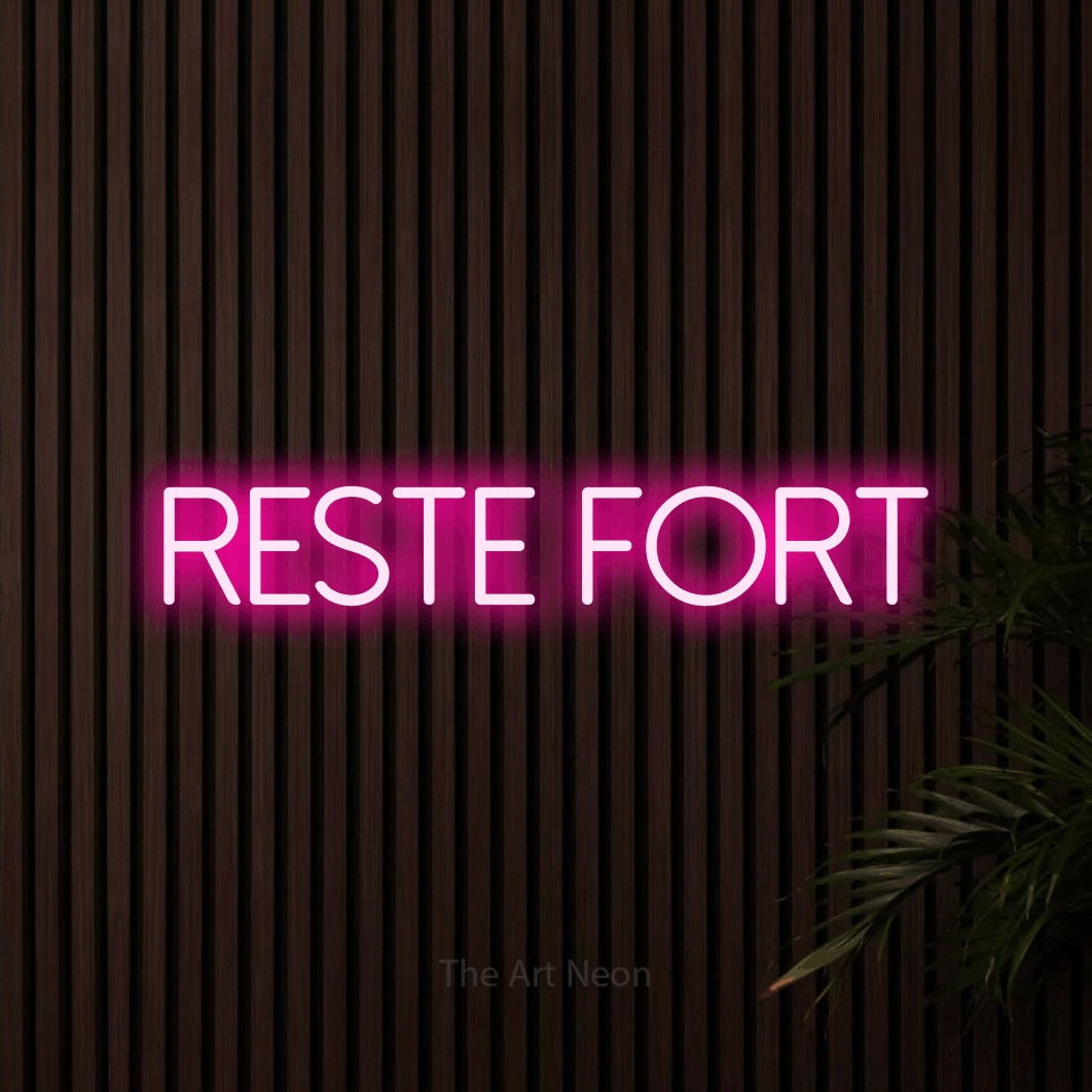 “Reste fort” LED neon sign in hot pink, with thin sans-serif lettering, shown against dark wooden wall slats.