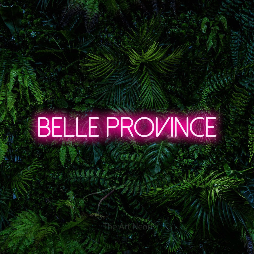 “Belle province” LED neon sign in hot pink, with thin sans-serif lettering, shown against dense tropical foliage.