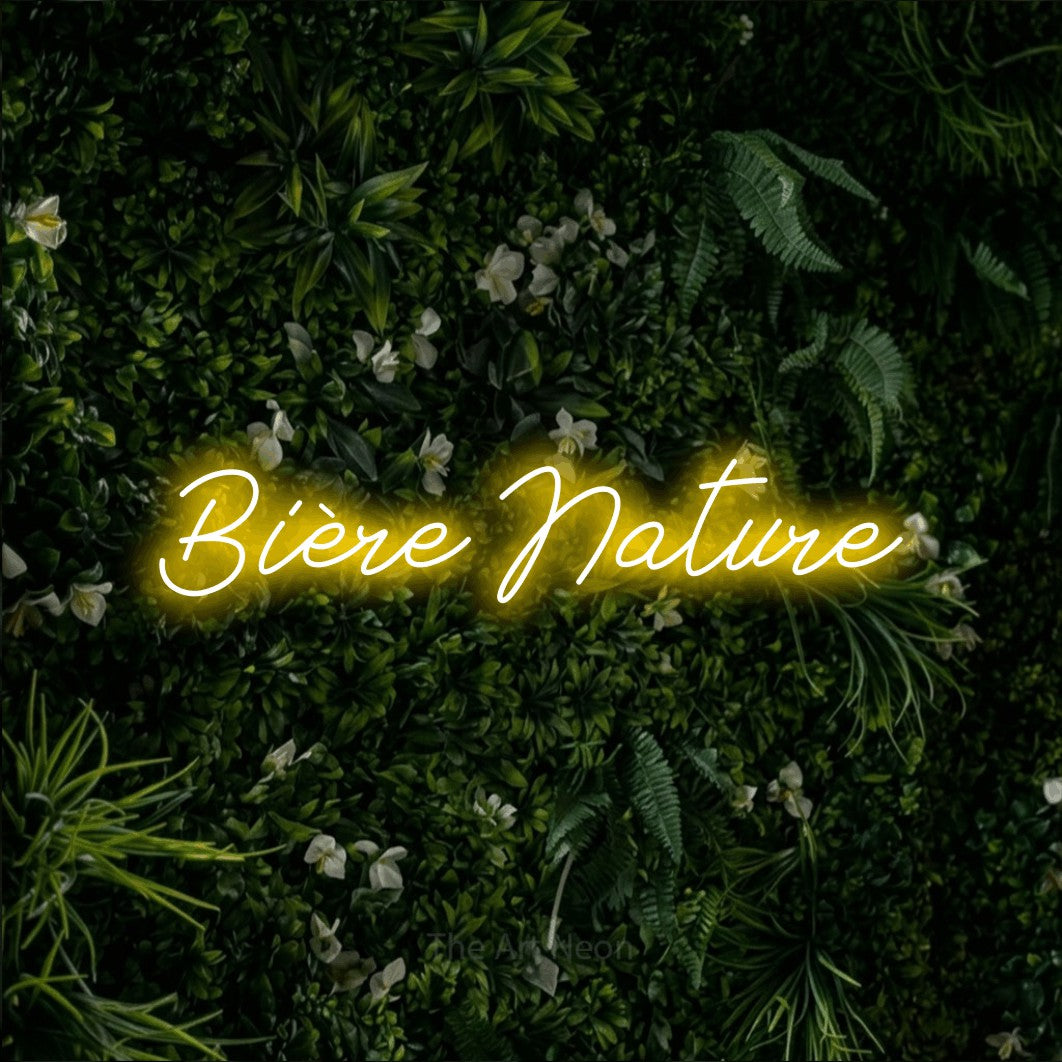 “Bière nature” LED neon sign in yellow, with cursive lettering, shown against a dense green plant wall.