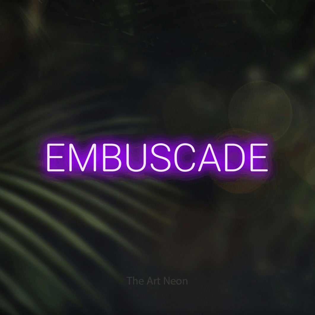 “Embuscade” LED neon sign in purple, with rounded sans-serif lettering, shown against a blurred palm and bokeh-light backdrop.