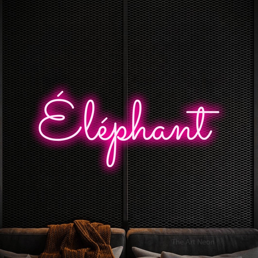 “Éléphant” LED neon sign in hot pink, with looped cursive lettering, shown against a modern dark-toned seating area.