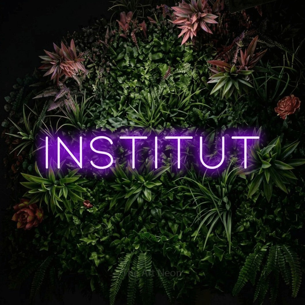 “Institut” LED neon sign in purple, with thin, widely spaced lettering, shown against a flowering plant wall.