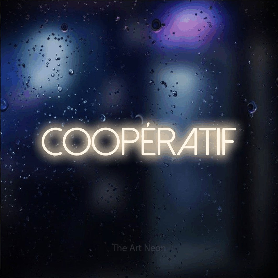 Néon LED « Coopératif » en blanc chaud, en lettres fines sans empattement, mis en scène sur une vitre aux reflets bleus et violets, pour un espace de jeux vidéo.