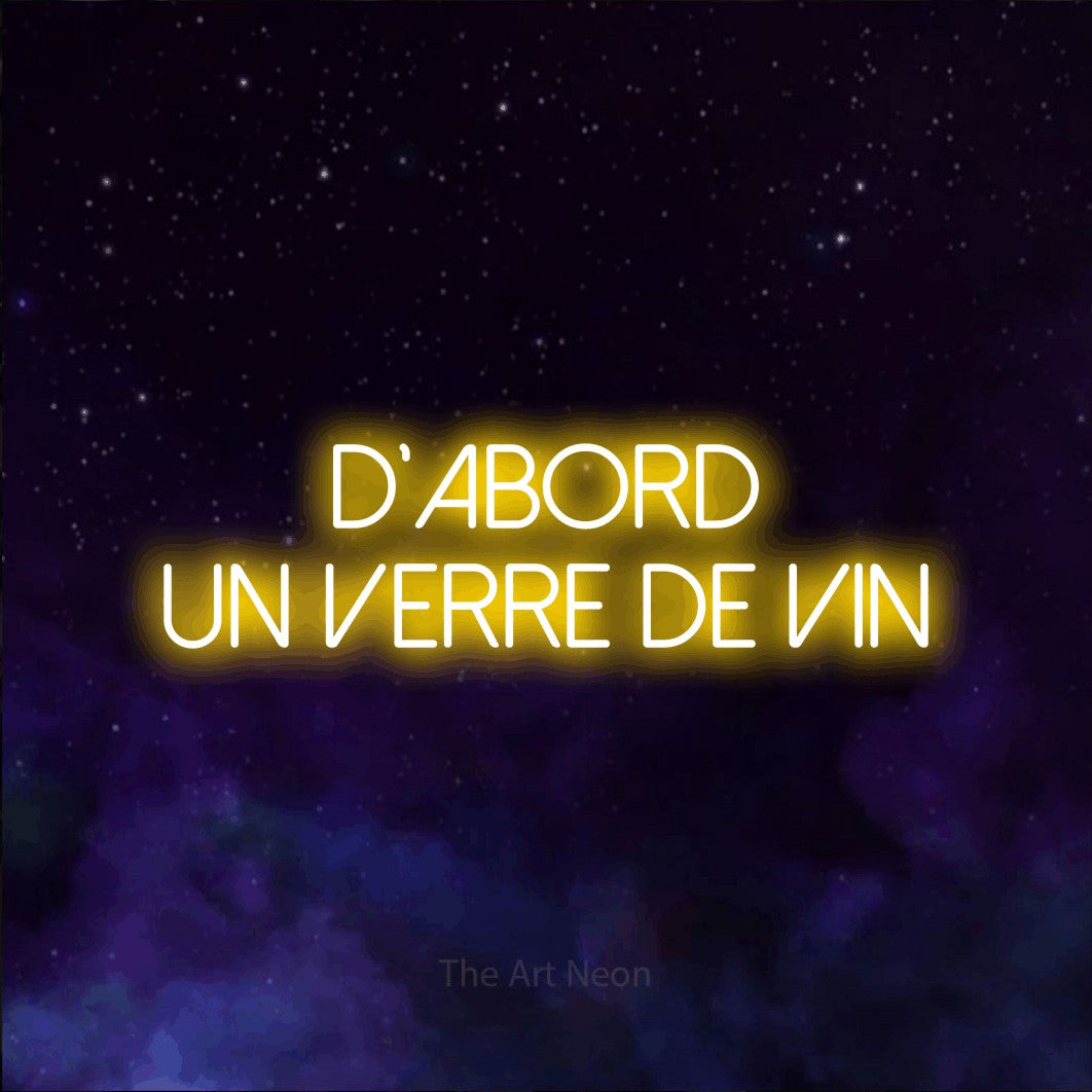 “D'abord un verre de vin” LED neon sign in yellow, with thin sans-serif lettering across 2 lines, shown against a purple galaxy backdrop.