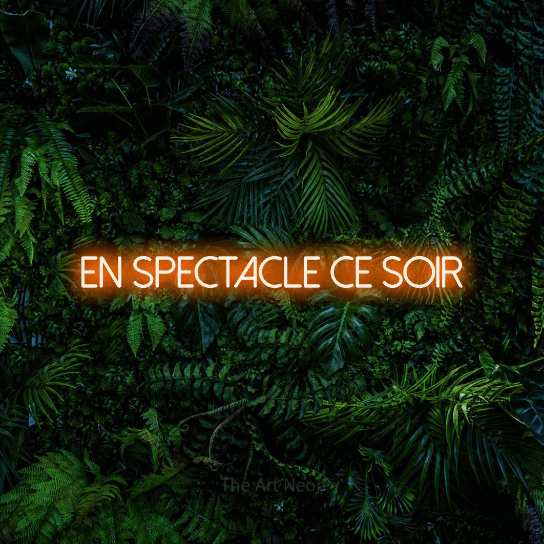 “En spectacle ce soir” LED neon sign in orange, with thin sans-serif lettering, shown against dense tropical foliage.