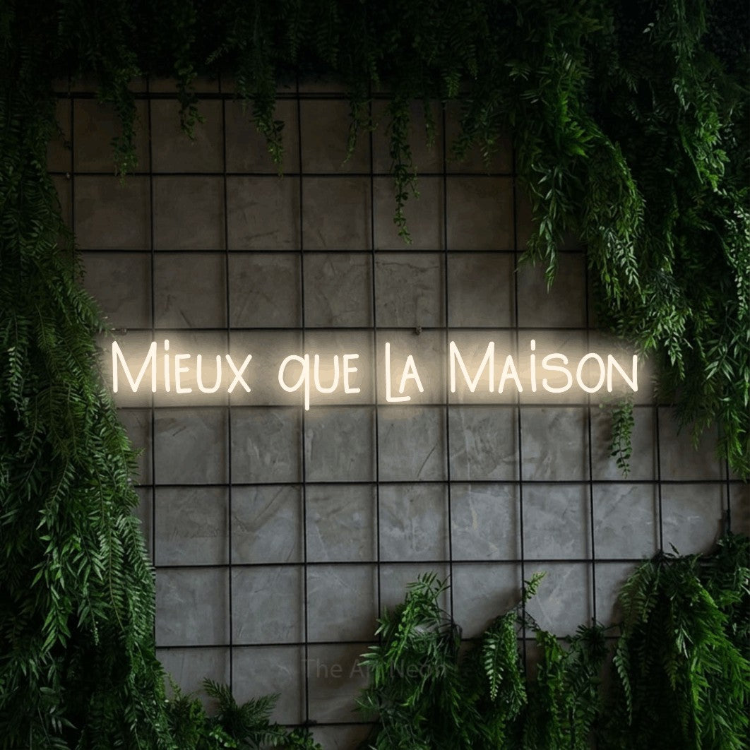“Mieux que la maison” LED neon sign in warm white, with narrow hand-drawn lettering, shown against an ivy-covered concrete grid.