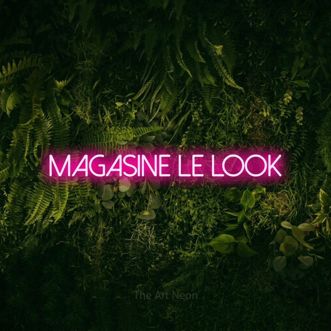 “Magasine le look” LED neon sign in hot pink, with thin sans-serif lettering, shown against a dark moss and forest backdrop.