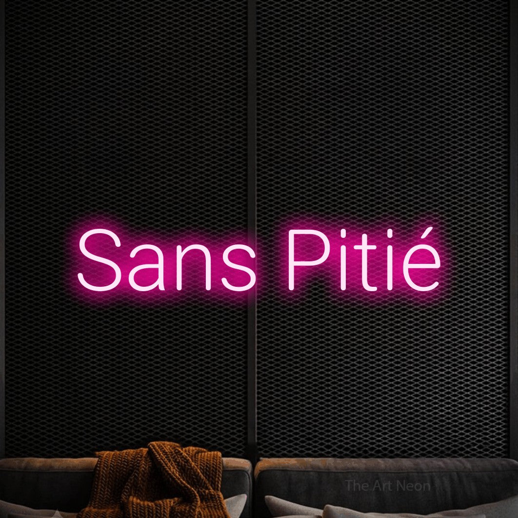 Lettrage en néon LED « Sans pitié » en rose vif, en lettres sans empattement arrondies, présenté dans un coin salon moderne aux tons noirs, pour un espace de jeux vidéo.