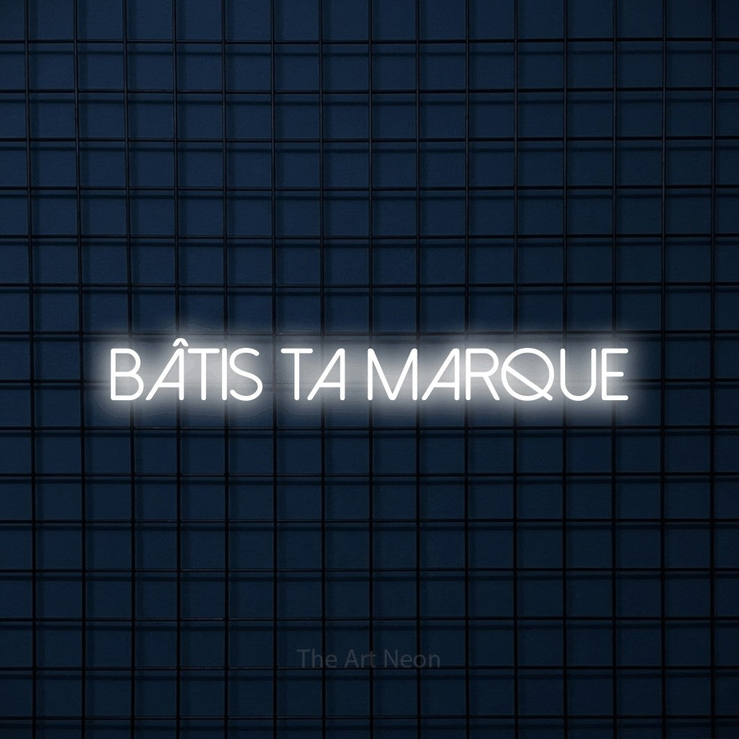 “Bâtis ta marque” LED neon sign in cool white, with thin sans-serif lettering, shown against a dark blue grid.