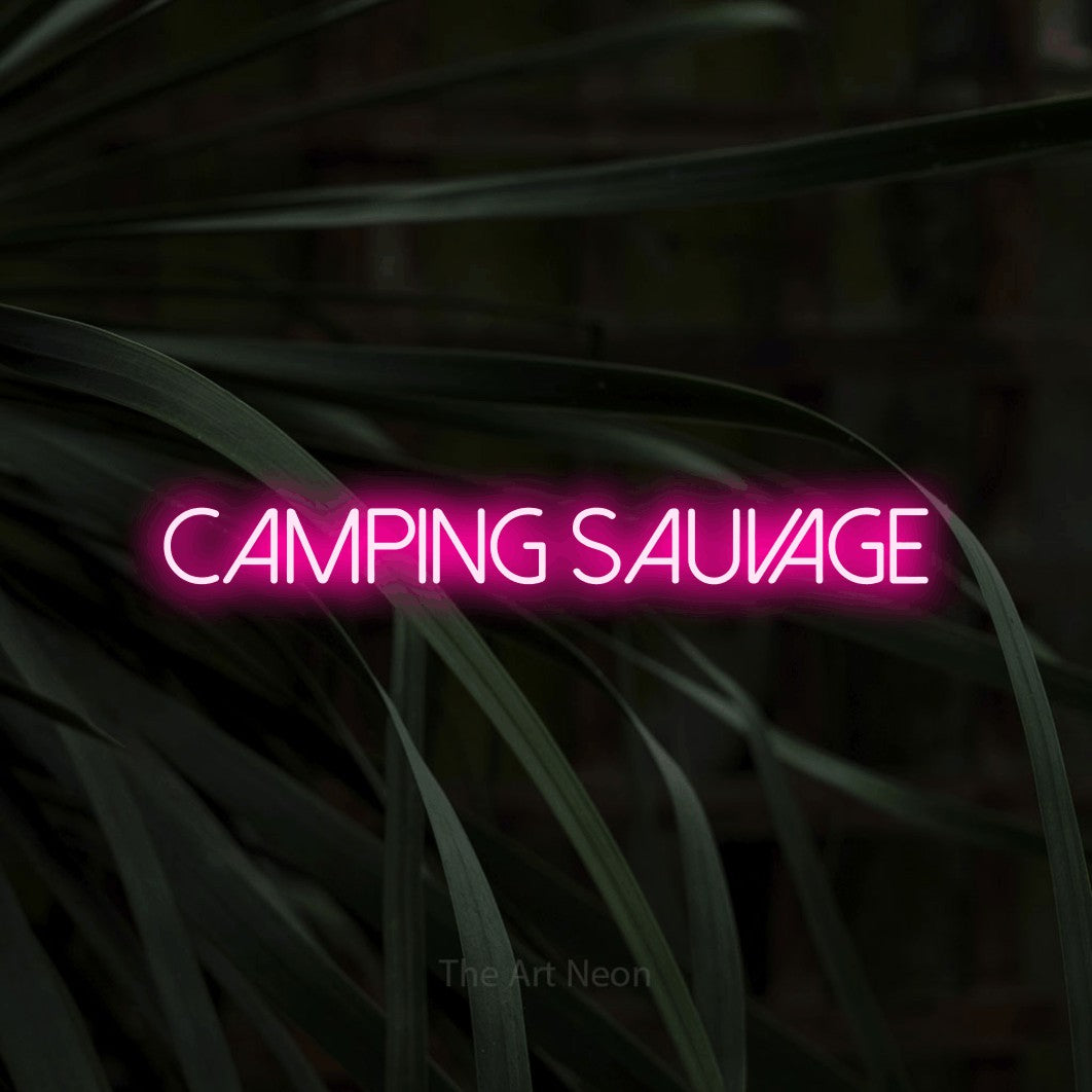 “Camping sauvage” LED neon sign in hot pink, with thin sans-serif lettering, shown against a close-up of dark foliage.
