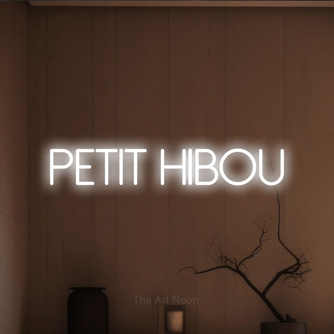 “Petit hibou” LED neon sign in cool white, with thin sans-serif lettering, shown against a simple earth-toned interior.