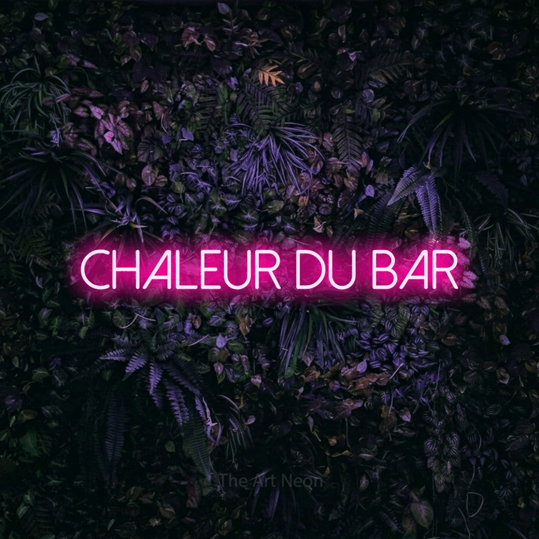 “Chaleur du bar” LED neon sign in hot pink, with thin sans-serif lettering, shown against a dark wall with purple flowers.