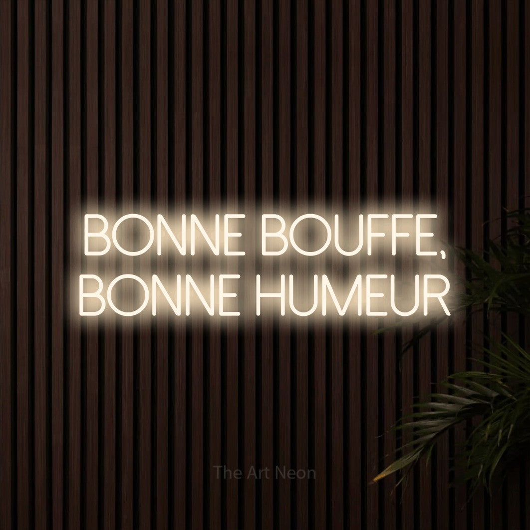 “Bonne bouffe, bonne humeur” LED neon sign in warm white, with thin sans-serif lettering across 2 lines, shown against dark wooden wall slats.