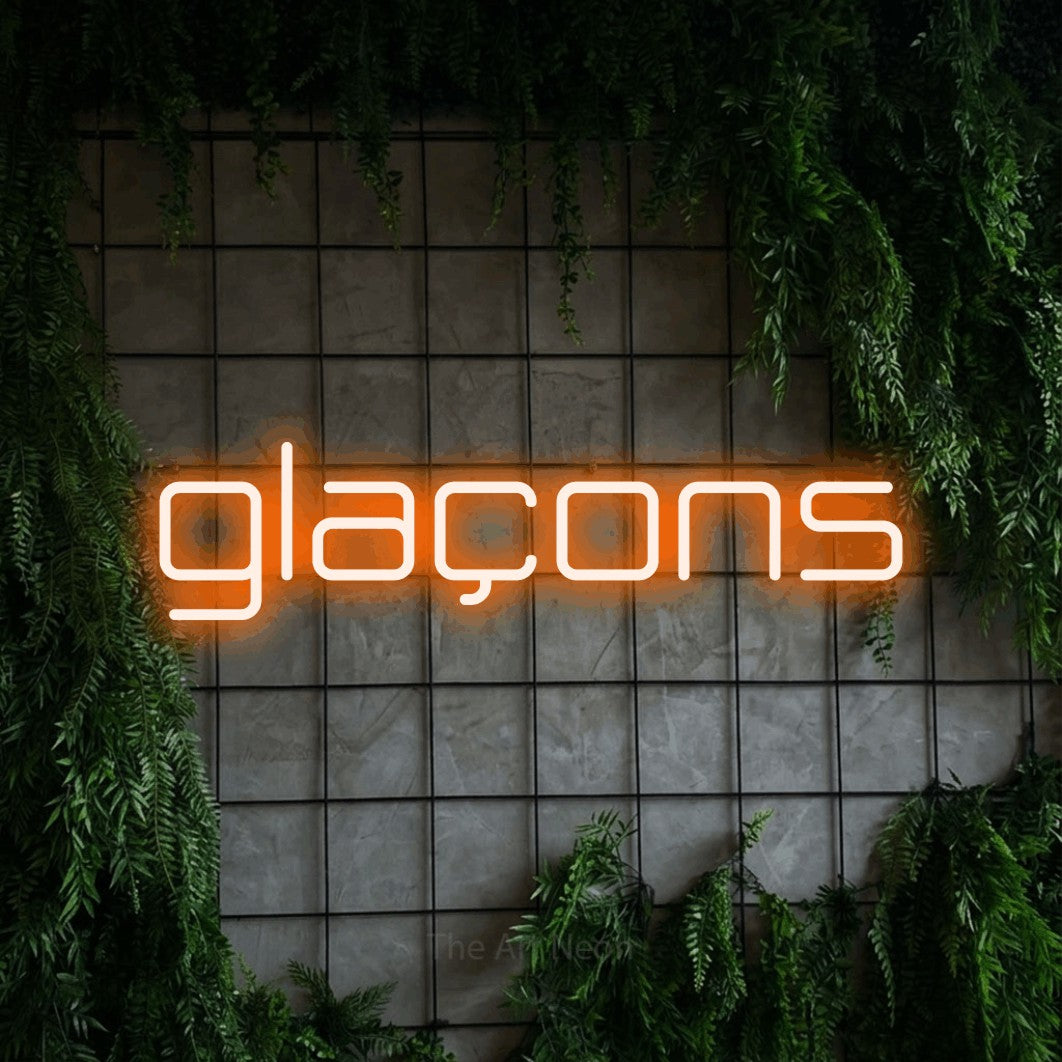 “Glaçons” LED neon sign in orange, with rounded geometric lettering, shown against an ivy-covered concrete grid.