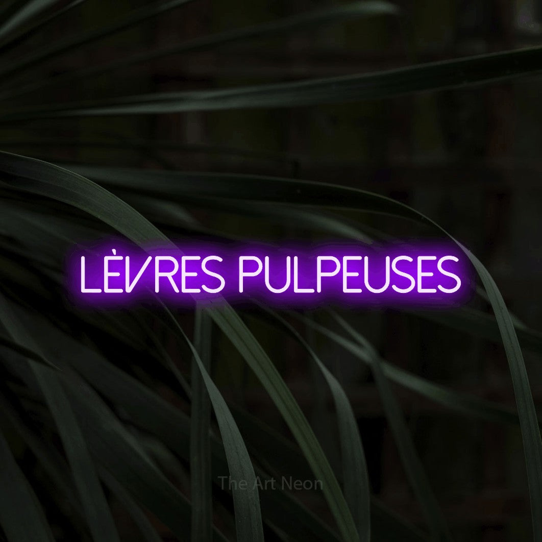 “Lèvres pulpeuses” LED neon sign in purple, with thin sans-serif lettering, shown against a close-up of dark foliage.