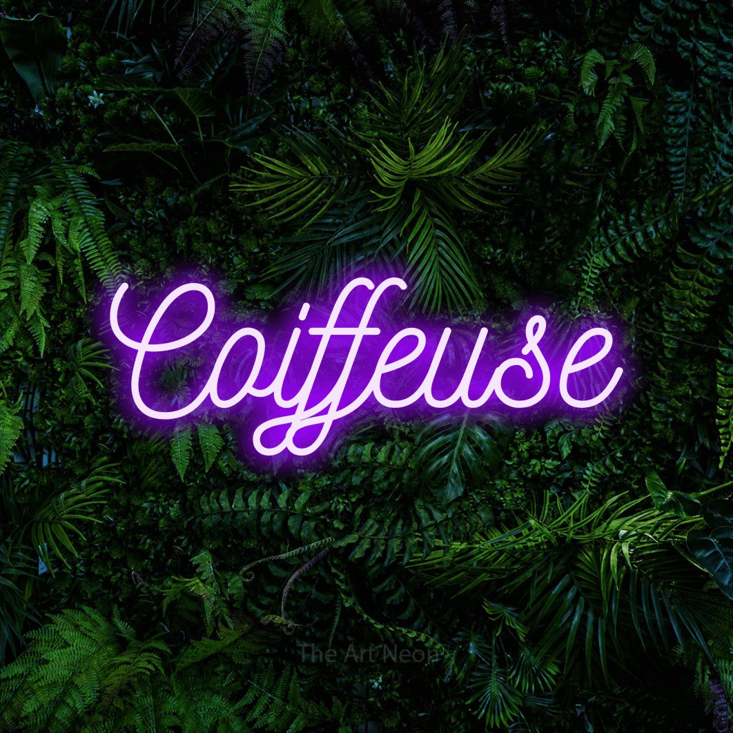 “Coiffeuse” LED neon sign in purple, with ornate cursive lettering, shown against dense tropical foliage.