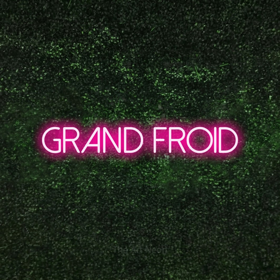 Décoration murale en néon LED « Grand froid » en rose vif, en lettres fines sans empattement, installée sur une haie verte texturée, pour un décor canadien.