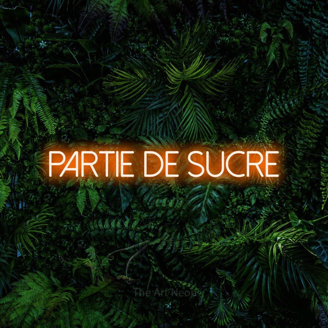 “Partie de sucre” LED neon sign in orange, with thin sans-serif lettering, shown against dense tropical foliage.