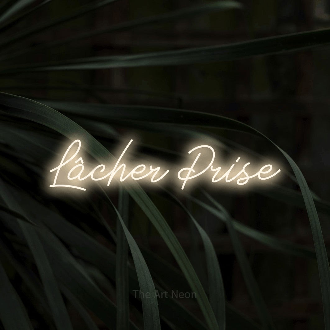 “Lâcher prise” LED neon sign in warm white, with cursive lettering, shown against a close-up of dark foliage.